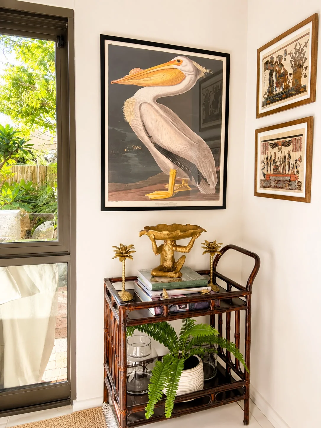 Pence House styling corner — bamboo bar cart, brass palm candlesticks and a framed Audubon pelican print